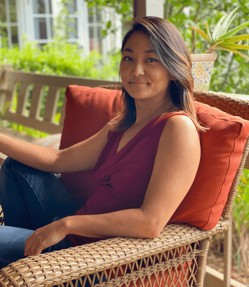 Lori Nishikawa, founder of Root to Reef, sitting on a lanai surrounded by plants